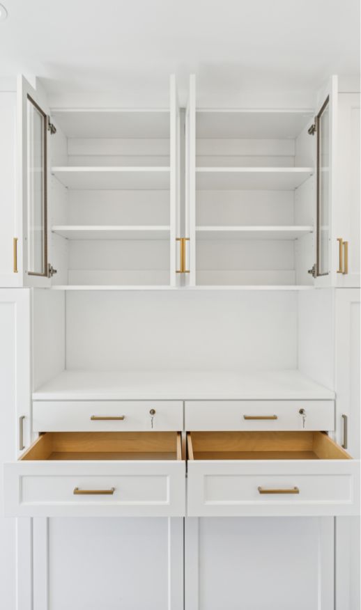 Open white kitchen cabinets and drawers with gold handles reveal empty shelves and interiors, set against a clean, bright background—perfect inspiration for custom closets designed by an expert custom closet designer.