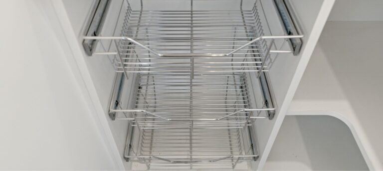 A close-up view of empty metal wire racks inside a white pull-out kitchen cabinet organizer.