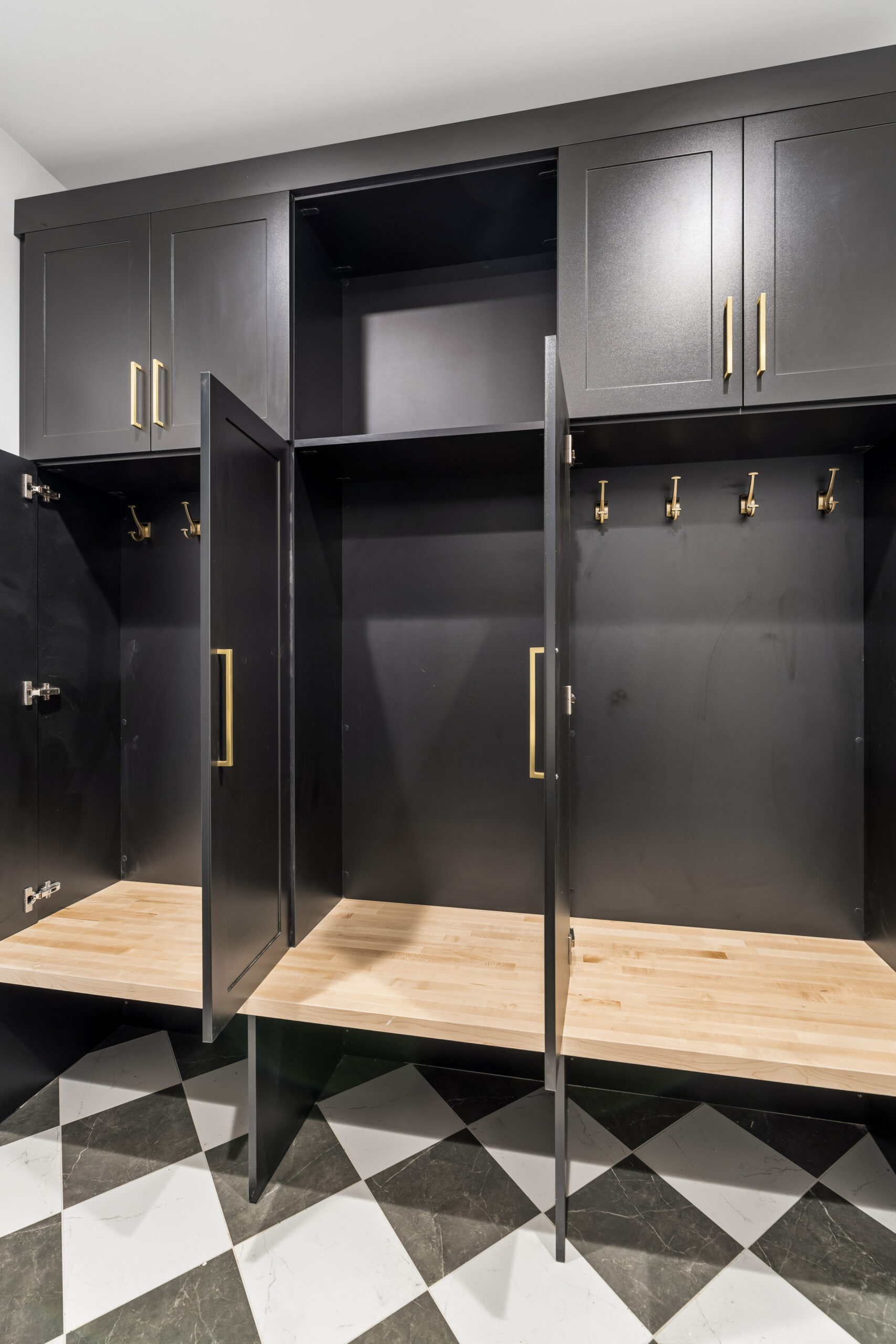 Open black cabinets with gold handles reveal wooden shelves and multiple coat hooks inside. The floor has a black and white checkered tile pattern. Upper cabinets are closed.