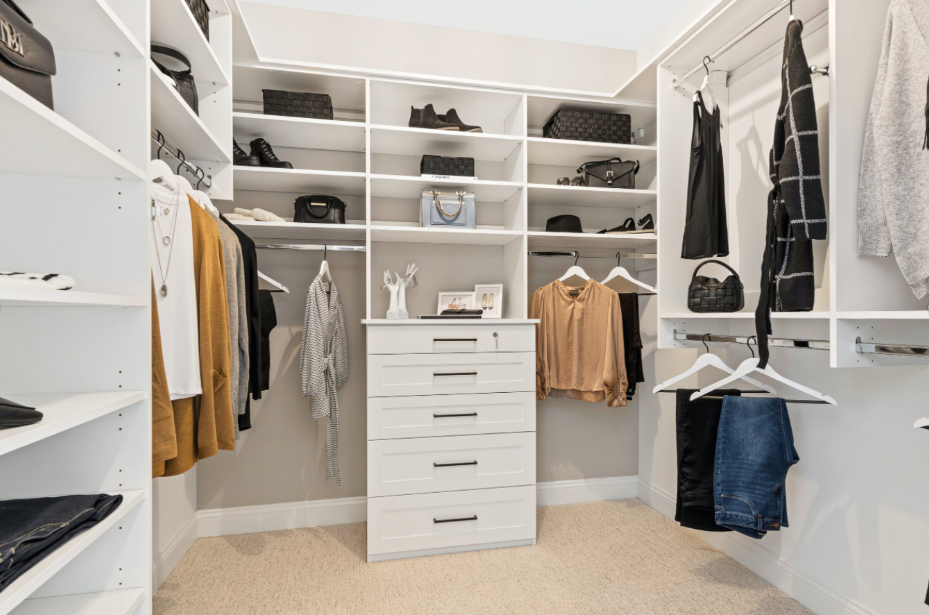 Walk-in closet with white shelving, a central chest of drawers, and hanging racks filled with organized clothing, handbags, and shoes.