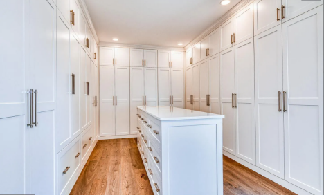 Walk-in closet with floor-to-ceiling white cabinetry and a central storage island over hardwood floors.