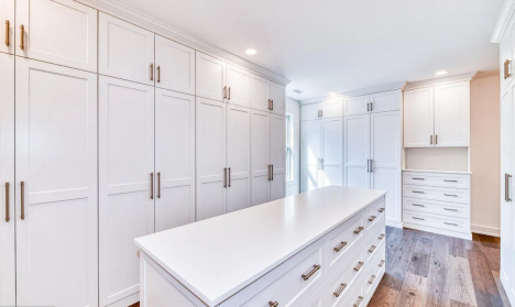 Walk-in closet with floor-to-ceiling white cabinetry, a large central island with drawers, and dark wood flooring.